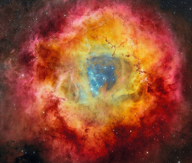 Stars on a dark blue background surrounded by clouds of a yellow, red and magenta nebula.