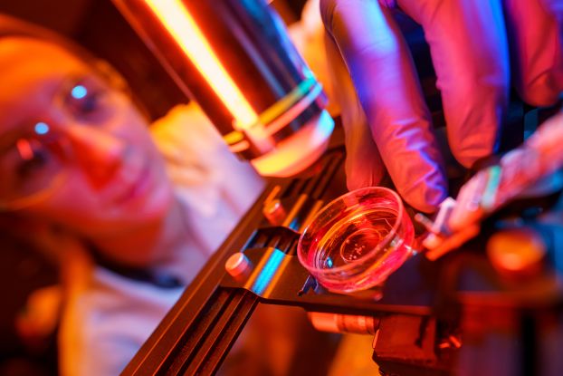 A closeup of a sample under a microscope with a researcher in the background.