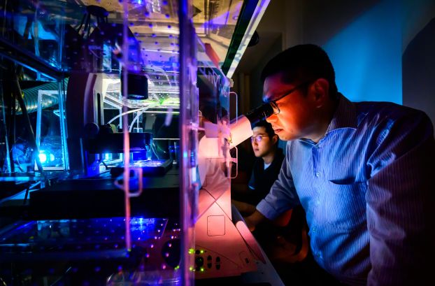 Researchers look into a microscope in a darkened room.