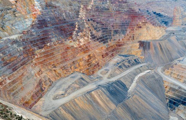 Terraced levels of red and brown rock in a mine with gray access roads and slopes below.