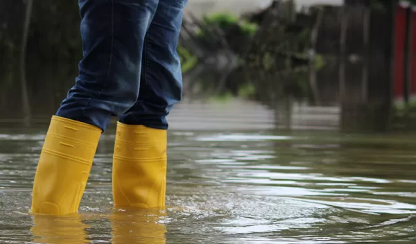 A person wearing yellow boots stands in flood water.