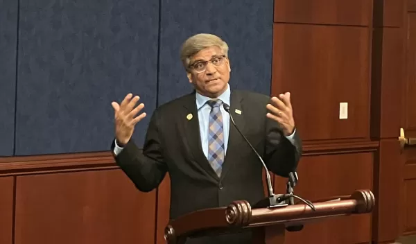 man in back suit and a pattern tie talking at a podium