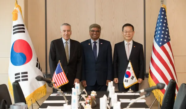 three men in suits standing in the middle of an American flag and Korean flag