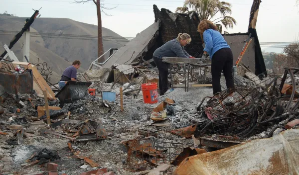 Two women sorting items on a table amongst piles of debris.