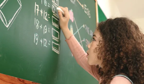 Young female student solving math equations at a chalkboard.