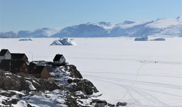 Houses overlooking the sea ice and icebergs. Note a small group of fishermen on the ice in the right of the image
