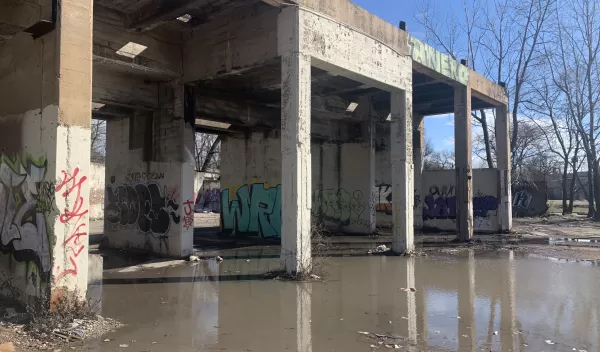 Standing water around the base of a concrete elevated train platform with graffiti on the support pillars.