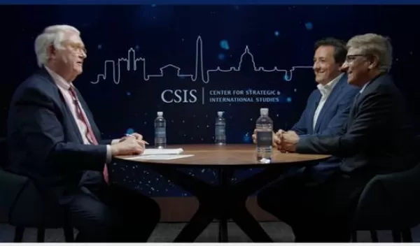 screenshot from a webinar with three men in suits sitting around a table