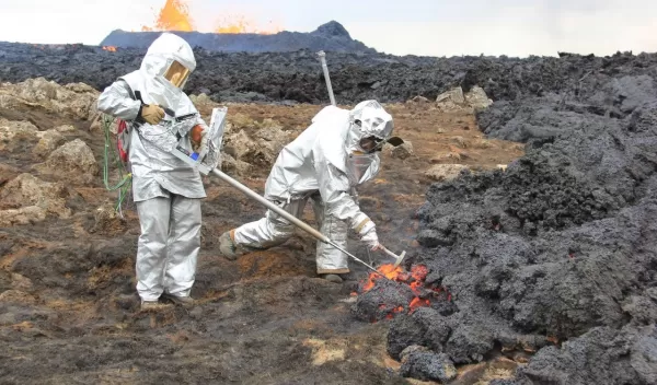 two men standing in a volcanic field wearing protective suits and masks