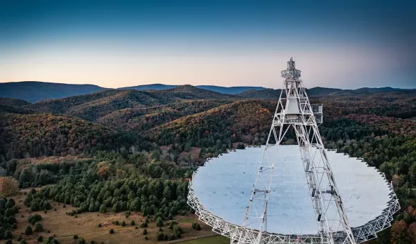 A large radio telescope high above green rolling hills.