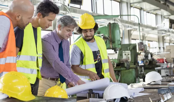 Male supervisor with workers discussing over blueprints in industry