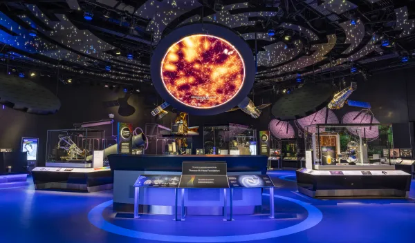A darkened exhibit hall with stars projected overhead and a large orange image in a circle in the middle.