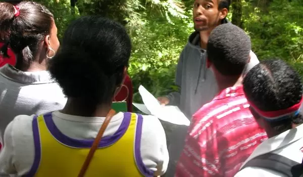 Photo of rapper C.A.U.T.I.O.N. engaging kids from Washington State exploring the forest environment.