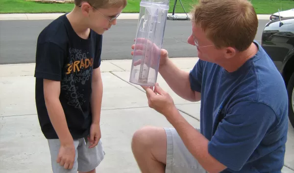 man and child look at a rain gauge in a driveway