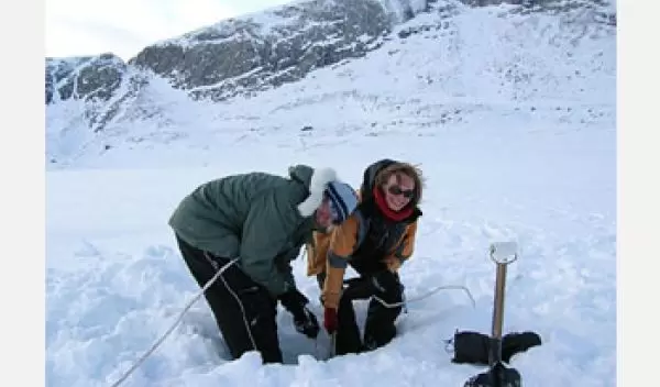 Photo shows 2 people collecting sediment core from a lake on Baffin Island.