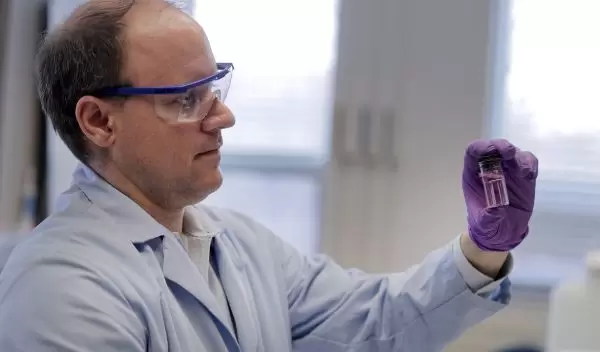 professor Andrew Whelton holds up a water sample from a building faucet