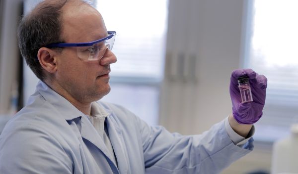 professor Andrew Whelton holds up a water sample from a building faucet