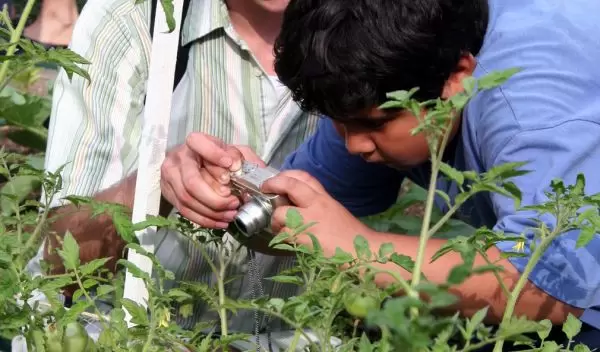 Man helps student aim digital camera at garden.