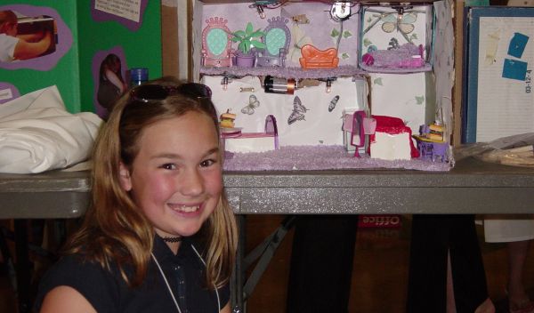 Young girl smiles at camera, science project in background.
