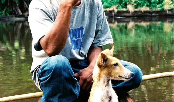 a Mayangna hunter and his dog resting in a dugout canoe.
