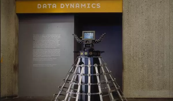 Child-sized robot meanders museum lobby, as people stare.