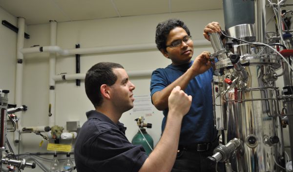 Photo of Ben Levinson watching Rama Balasubramanian adjust the levels of gases in a fermenter.