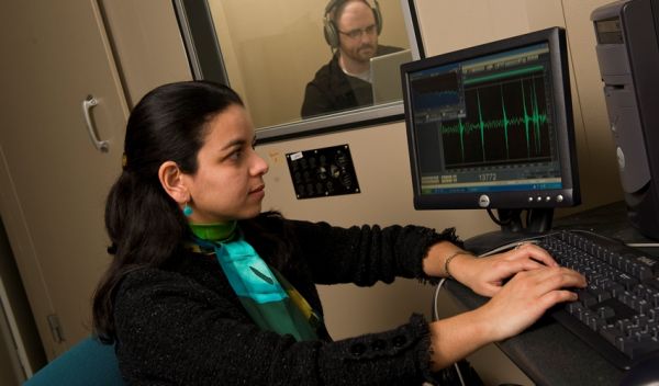 Photo of researcher and a colleague in a sound booth using a computer to record sound