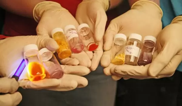 Photo of hands holding conjugated polymers that change color and intensity when excited by light.