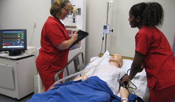 Nurses next to a robotic patient in a hospital bed
