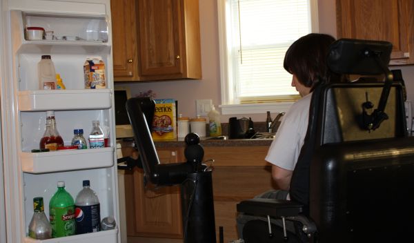 Photo of person with disabilities piloting a robotic mobility and manipulation system in kitchen.