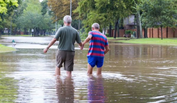 Two men walk hand in hand through a flood-covered street.
