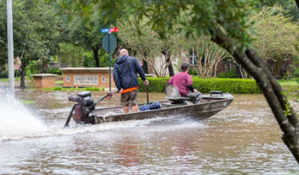 Two men in motorboat traveling along flood-covered street.