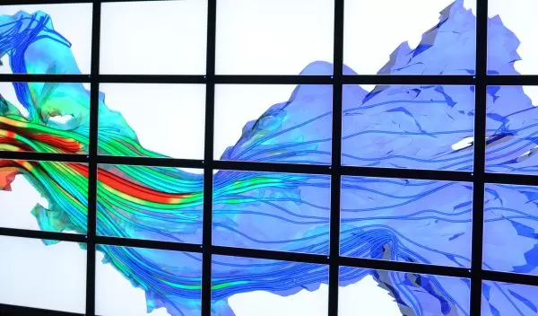 A young man stands in front a bank of computer monitors that project a simulation of river currents.