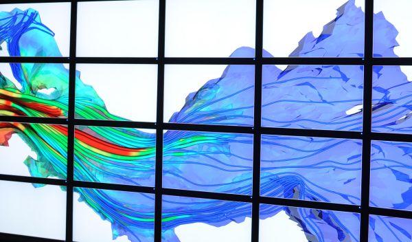 A young man stands in front a bank of computer monitors that project a simulation of river currents.