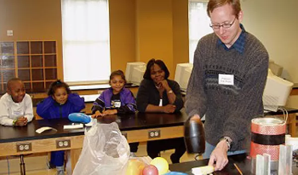 Researcher is about to smash a banana while several children and an adult watch the demonstration.