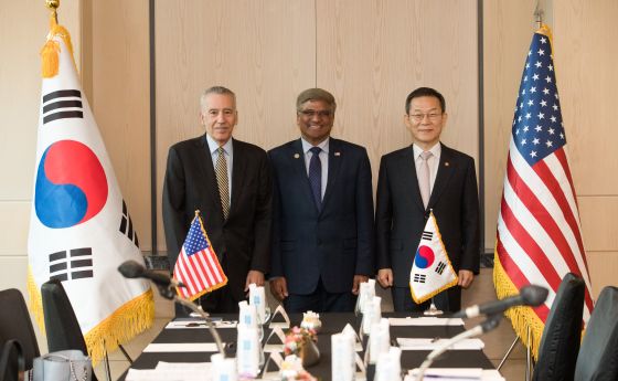 three men in suits standing in the middle of an American flag and Korean flag