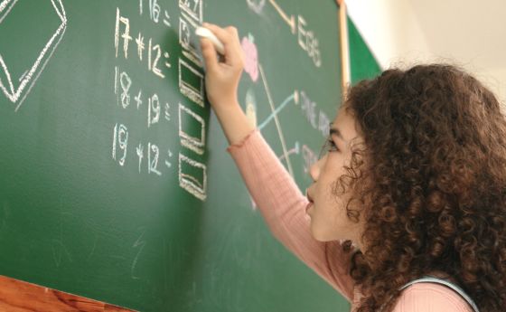 Young female student solving math equations at a chalkboard.