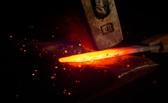 Red hot piece of metal is held by tongs and struck by a big hammer.