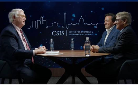 screenshot from a webinar with three men in suits sitting around a table