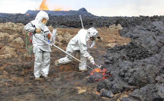 two men standing in a volcanic field wearing protective suits and masks