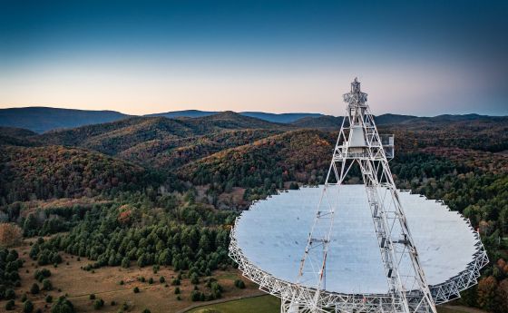 A large radio telescope high above green rolling hills.