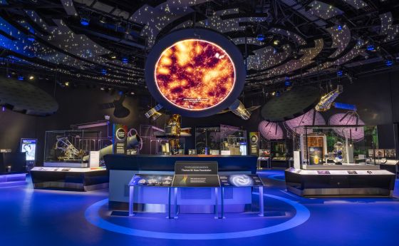 A darkened exhibit hall with stars projected overhead and a large orange image in a circle in the middle.