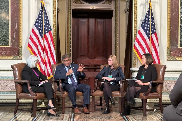 White House Office of Science and Technology Policy Director Arati Prabhakar, NSF Director Sethuraman Panchanathan, NIST Director Laurie Locascio, and ARPA-H Director Renee Wegrzyn sit in together in armchairs between two American flags.