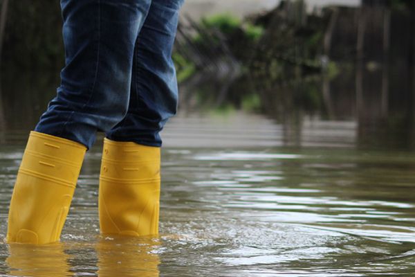 A person wearing yellow boots stands in flood water.