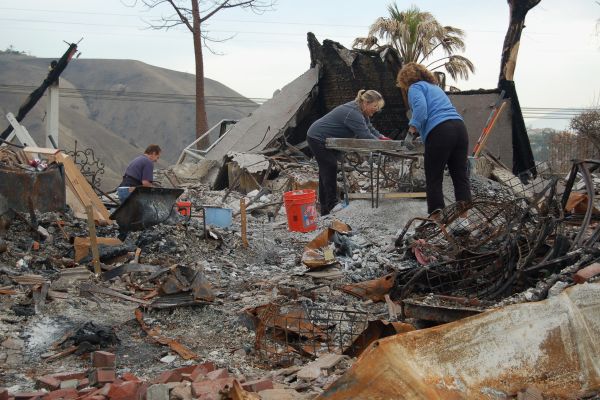 Two women sorting items on a table amongst piles of debris.