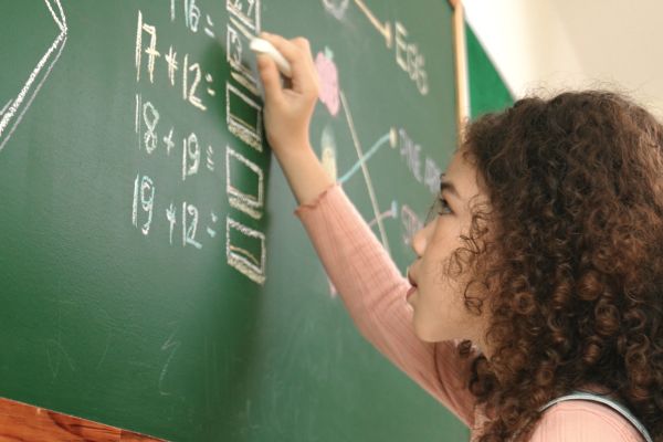 Young female student solving math equations at a chalkboard.