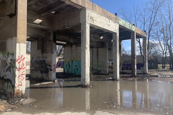 Standing water around the base of a concrete elevated train platform with graffiti on the support pillars.