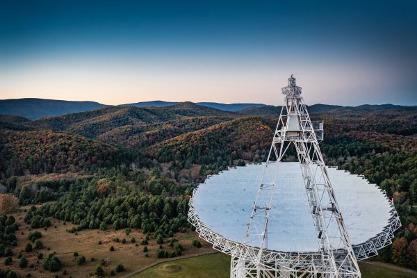 A large radio telescope high above green rolling hills.