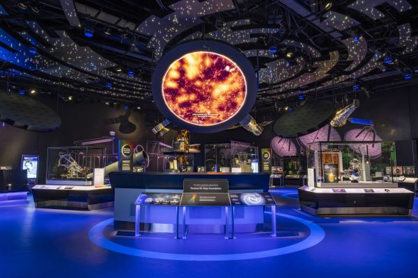 A darkened exhibit hall with stars projected overhead and a large orange image in a circle in the middle.